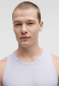 Top senza maniche di un leggero lavanda, realizzato in un tessuto morbido e texturizzato. Collo rotondo e dettagli di cucitura minimali, indossato da un modello con capelli corti.