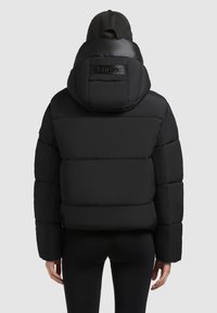 Juodas pūkuotas paltas su gobtuvu, siuvinėtas, dideliu siluetu. Yra logotipo priklijuota etikete ant nugaros ir audinio rankogaliai.