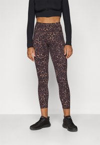 Legginsy w stylu body w brązowo-czarny wzór w panterkę, z wysokim stanem i dopasowanym krojem, w zestawieniu z czarnymi butami sportowymi.
