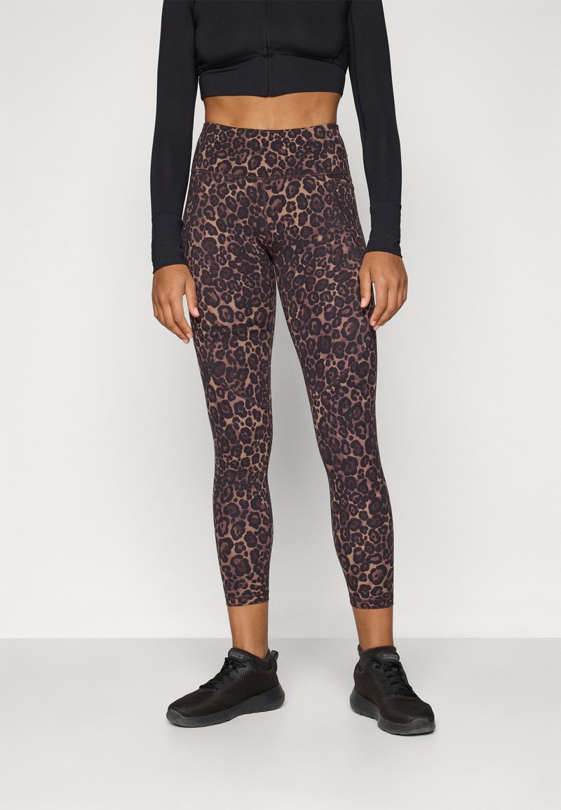 Legginsy w stylu body w brązowo-czarny wzór w panterkę, z wysokim stanem i dopasowanym krojem, w zestawieniu z czarnymi butami sportowymi.