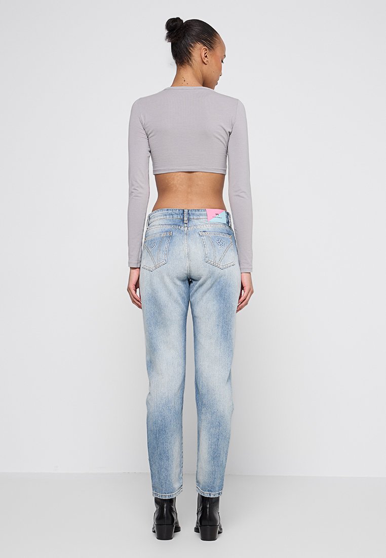 Mujer con el cabello recogido en un moño, vistiendo una camiseta cropped de manga larga gris, unos vaqueros de tiro alto azul claro con bordados de estrellas, y botas negras de tobillo, de pie.
