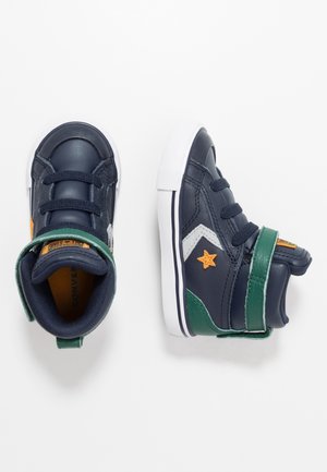 Mørkeblå sneakers til småbørn med hvide såler, grønne stropper, orange stjernebesætninger og sorte snørebånd, vist fra top- og sidevinkler.