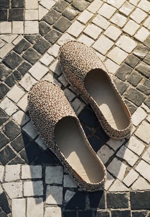 Ein Paar Slipper mit Leopardenmuster auf schwarz-weiß gemusterten Mosaikfliesen.