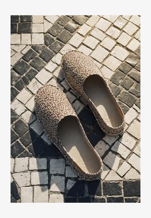 Ein Paar Slipper mit Leopardenmuster auf schwarz-weiß gemusterten Mosaikfliesen.