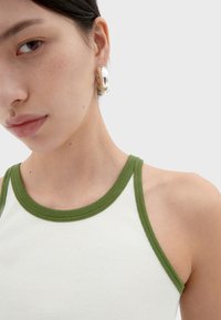 White ribbed tank top with green trim, featuring a close-up of a model’s neck and earring, showcasing smooth skin and silver hardware.