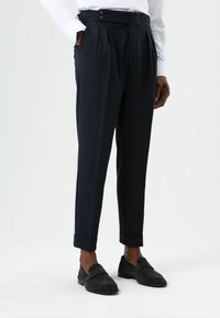 Marineblauwe op maat gemaakte broek met plooien, omgeslagen zoom en zijzakken. Gemaakt van een gestructureerde stof, met twee knopen op de tailleband.