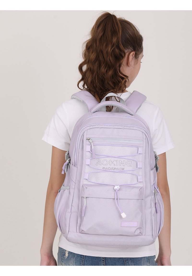 Zaino lilla chiaro con spalline imbottite regolabili, scomparti multipli con zip, dettagli in rete e una finitura in tessuto testurizzato.