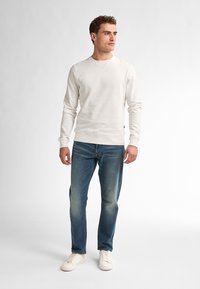 Light beige sweatshirt with speckled texture, crew neckline, and ribbed cuffs, paired with blue denim jeans and white sneakers.