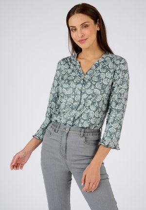 Grüne blumengemusterte Bluse mit Knopfverschluss und langen Ärmeln, versehen mit Rüschensäumen und einem Kragen, kombiniert mit grauen High-Waist-Jeans.