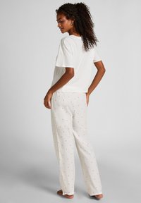 Λευκό βαμβακερό κοντομάνικο μπλουζάκι σε συνδυασμό με παντελόνια εκρού χρώματος με μικρά κόκκινα μοτίβα καρδιάς. Άνετη εφαρμογή και απαλό ύφασμα.