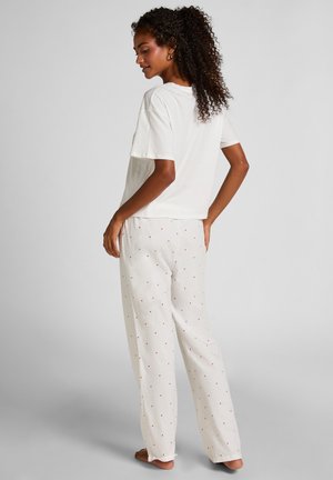 Weißes Baumwoll-T-Shirt mit kurzen Ärmeln, kombiniert mit cremefarbenen Hosen mit kleinen roten Herzmustern. Bequeme Passform und weiche Textur.