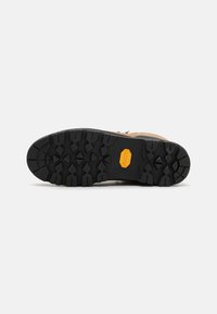 Brun tursko såle med svart gummibunn fra Vibram som har dype mønster for godt grep og en synlig logo. Teksturert overflate.