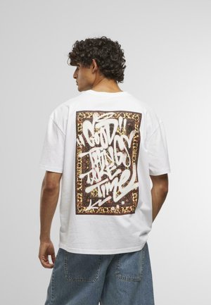 White cotton t-shirt featuring a large graphic print on the back with bold white graffiti text on a brown, patterned background.