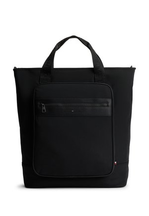 Black tote bag with two handles, large front zippered pocket with textured trim, and small red, white, and blue flag detail on pocket edge.