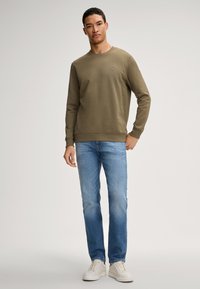 Oliwkowa bluza z okrągłym dekoltem, z prążkowanymi mankietami i dołem. Połączona z jasnoniebieskimi dżinsami i białymi butami sportowymi. Prosty, codzienny wygląd.