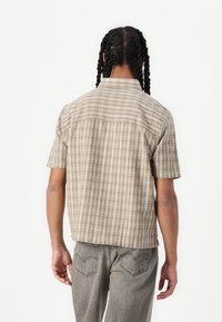 Camicia a maniche corte a quadri in tonalità beige, con colletto, taglio squadrato e un tessuto leggermente strutturato.