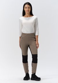 Beige active pants with black knee patches, elastic waistband, and zippered side pockets; paired with a white long-sleeve top and black shoes.