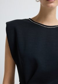 Top nero con un design strutturato sulle spalle, tessuto morbido e un'elegante decorazione argentata lungo lo scollo.