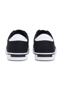 Μαύρα πάνινα παπούτσια με λευκή λεπτομέρεια στη φτέρνα, υφή επιφάνειας και λευκή καουτσούκ σόλα με μαύρο λογότυπο στο πλάι.