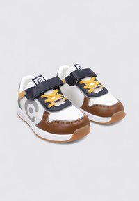 Baskets avec un dessus en cuir blanc et marron, une sangle en velcro bleu marine, des lacets jaunes et un logo gris sur le côté. Semelle en caoutchouc.