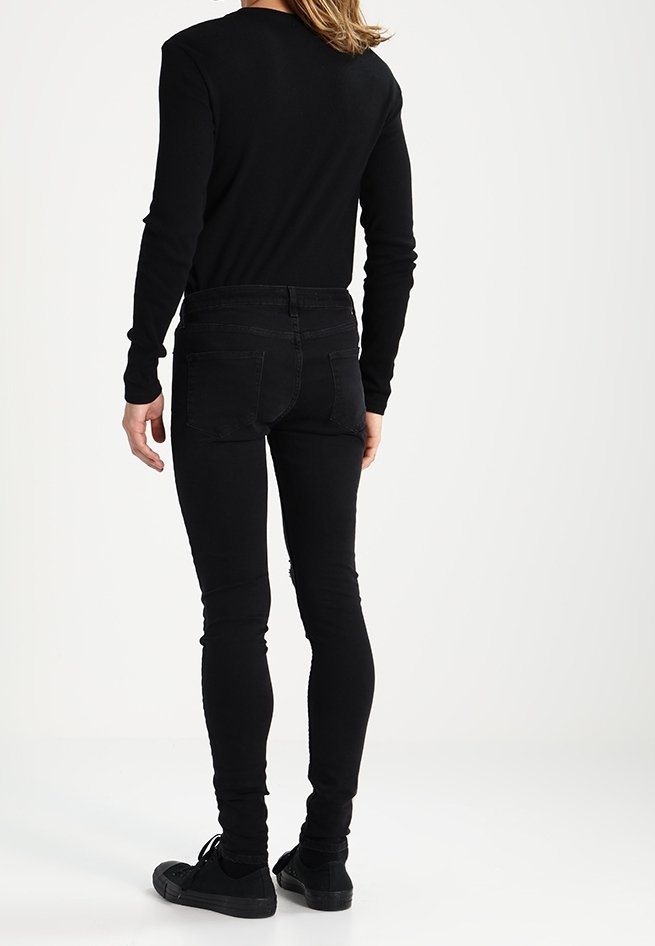 Jeans ajustados negros con una textura suave, dos bolsillos traseros y un diseño de cintura media, combinados con una camiseta negra de manga larga y zapatillas negras.