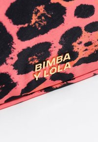 Acercamiento de una tela de estampado de leopardo en rosa y negro con detalles en dorado del logo "BIMBA Y LOLA" en el borde inferior.