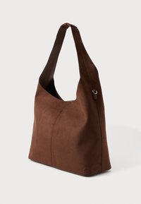 Καφέ σουέτ τσάντα ώμου με φαρδιά καμπύλη θηλιά, η οποία διαθέτει ραφές και απαλή υφή για μια δομημένη αλλά ταυτόχρονα χαλαρή εμφάνιση.