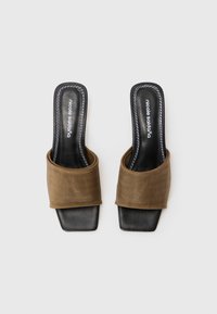 Brown fabric mules with a wide strap, square toe, and black sole. Features white stitching on the insole. Flat and open design.