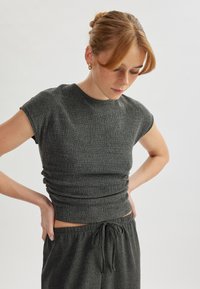 Top ajustado de color gris oscuro con una tela texturada de canalé y mangas cortas. Combinado con pantalones de tiro alto a juego que cuentan con cordón.