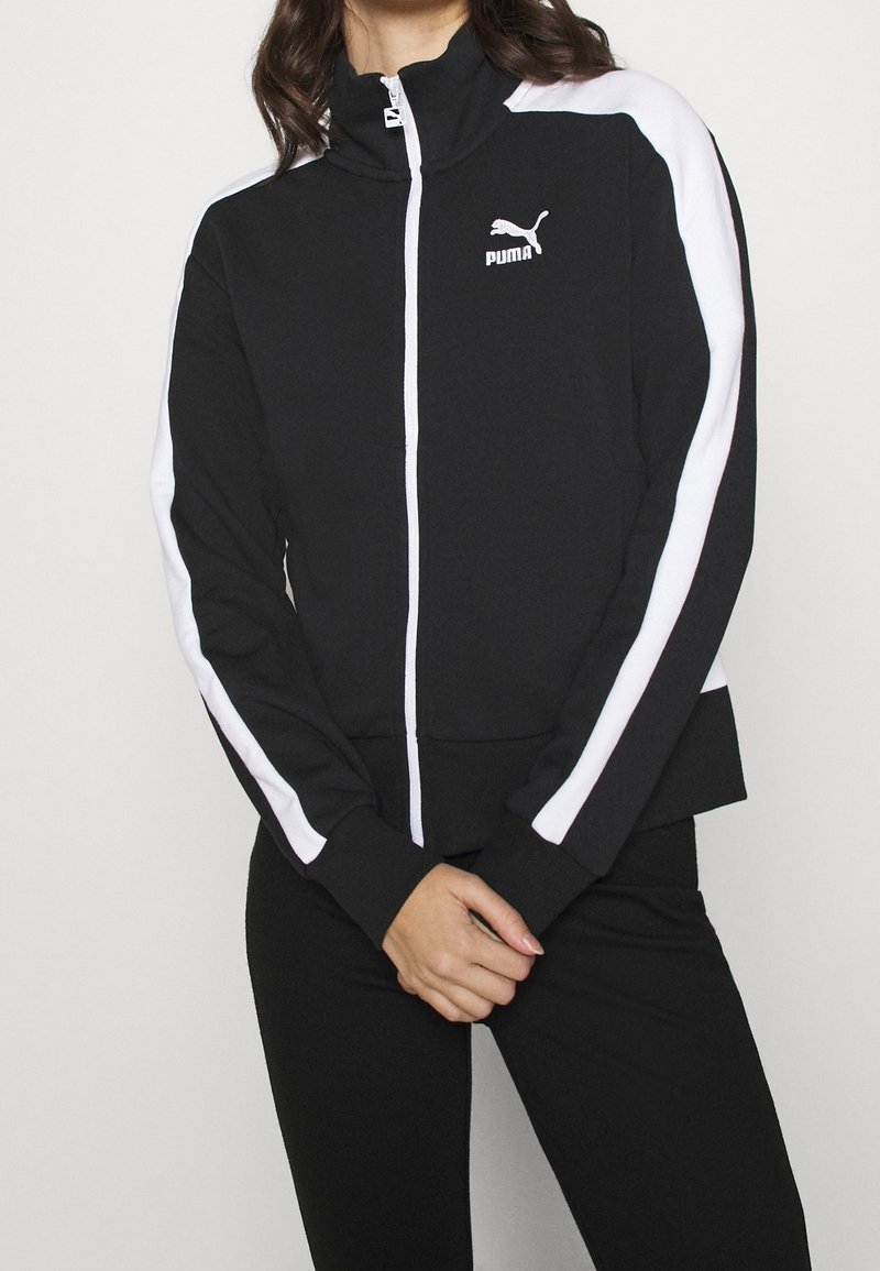 Sort zip-jakke med høj krave, hvide sidepaneler og Puma-logo. Har en tætsiddende design samt ribbede manchetter og kant.