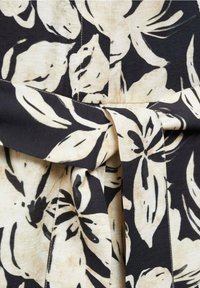 Gros plan sur un tissu noir et beige avec un grand imprimé floral abstrait et un détail de ceinture nouée au centre.