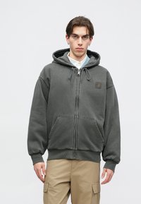 Γκρι φούτερ με φερμουάρ και κουκούλα με κορδόνι, μπροστινές τσέπες και ρεβέρ στον καρπό. Φτιαγμένο από μαλακό ύφασμα, με λογότυπο στη θήκη του στήθους.