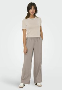 Beige kortærmet striktop parret med løstsiddende, lysebrune, plisserede bukser og hvide sportsko. Enkel, afslappet design.