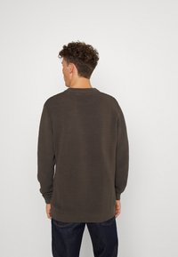 Pulover maro supradimensionat, cu model ribbed, guler rotund și mâneci lungi; textură netedă cu o croială lejeră, asortat cu blugi închisi.