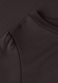 Gros plan d'un tissu marron foncé montrant un col côtelé et un détail d'emmanchure bouffante.