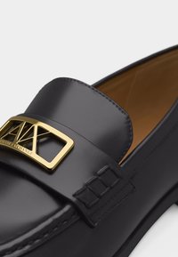 Μαύρος δερμάτινος μοκασίνι με χρυσή λεπτομέρεια λογότυπου Armani Exchange στο λουράκι και ταμπά εσωτερική επένδυση από δέρμα.