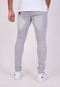 Vaqueros skinny de color gris claro con una textura suave, diseño de cinco bolsillos y detalles de costura sutiles. Par de zapatillas blancas con un logo.