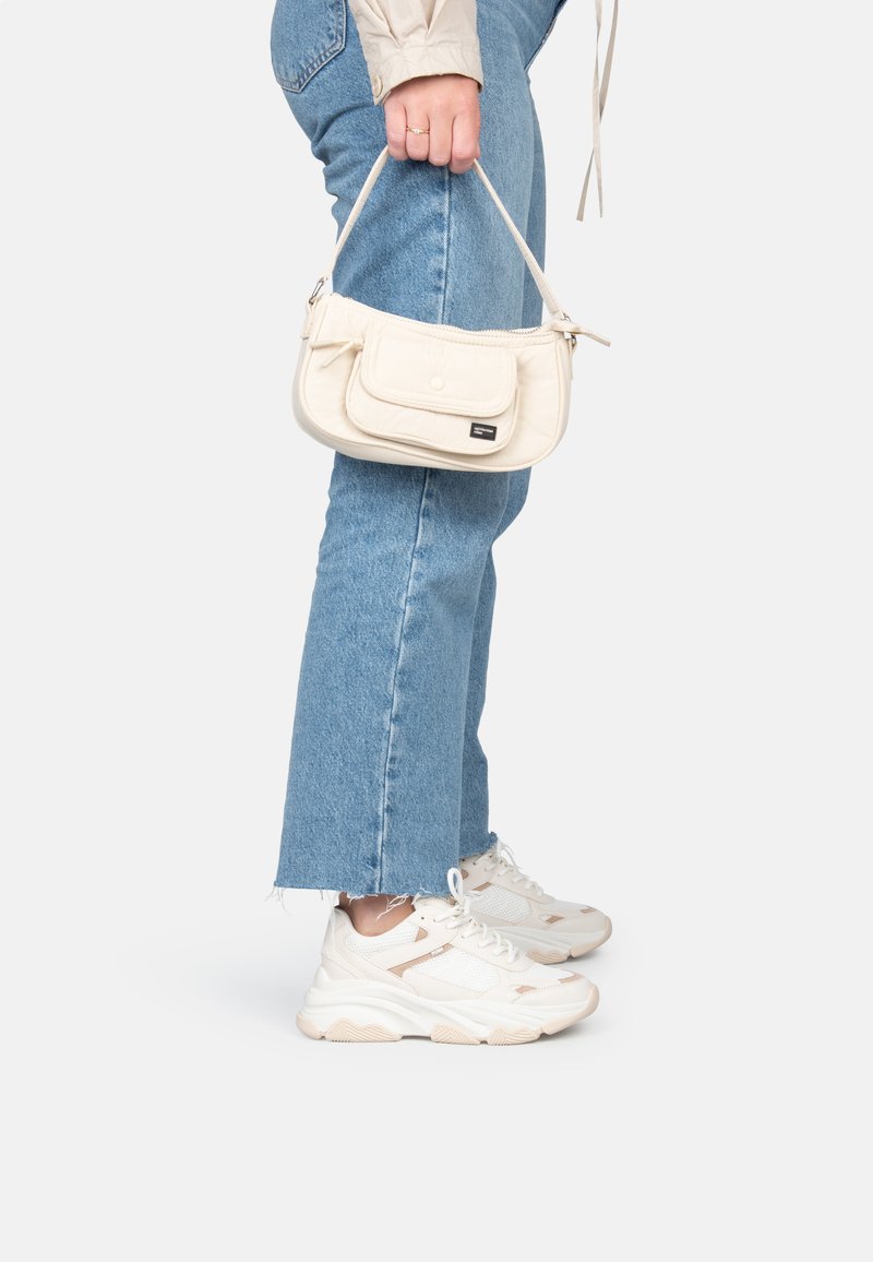 Bolso blanco acolchado con un bolsillo delantero y cierre de botón, combinado con jeans de pierna recta azul claro y zapatillas blancas con detalles beige.