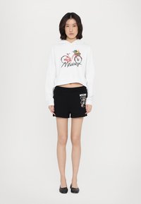 White cropped hoodie with bicycle graphic and "Moschino" text, paired with black shorts featuring a teddy bear design and logo.