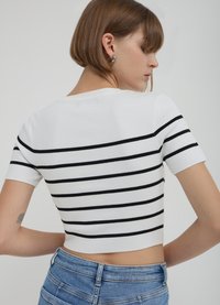 Weißes, geripptes, kurz geschnittenes Oberteil mit schwarzen, horizontalen Streifen, kurzen Ärmeln und rundem Ausschnitt. Kombiniert mit hoch taillierten Jeans aus Denim.