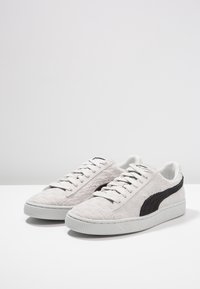 Vaaleanharmaat lenkkarit, jotka on valmistettu texturoituneesta materiaalista. Niissä on musta sivupaneeli, pyöreä kärki ja valkoinen kumipohja, jossa on vaakasuorat urat.