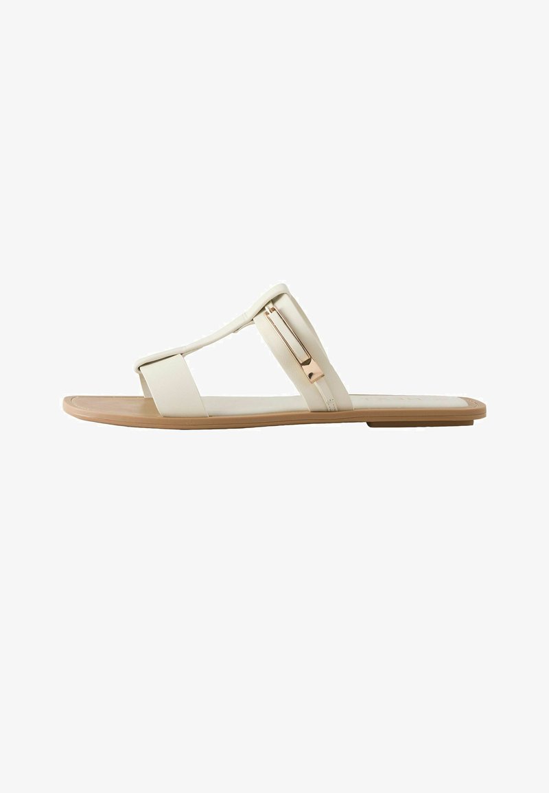 Sandale à glissière plate beige avec deux larges brides et une boucle rectangulaire métallique sur la bride supérieure, sur une semelle en bois clair.