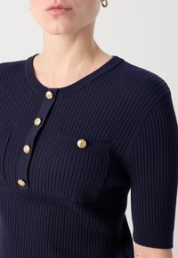 Granatowy prążkowany dzianinowy top z krótkimi rękawami, z okrągłym dekoltem, złotymi guzikami z przodu i dwoma kieszeniami na przodzie.