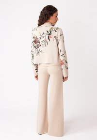 Beige gebreide trui met florale borduring in roze, rood en groen. Gecombineerd met bijpassende beige wijde broek met een geribbelde tailleband.