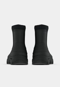 Bottes de cheville noires étanches en matériau lisse et texturé, avec une tige haute et une semelle en caoutchouc robuste pour une meilleure adhérence.