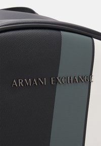 Zaino a strisce nere e verdi con superficie testurizzata e dettagli lisci. Presenta il logo "Armani Exchange" in nero in rilievo.