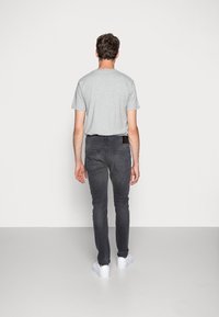 Camiseta gris de manga corta, jeans ajustados gris oscuro, zapatillas blancas, diseño minimalista, costura estándar, sin logotipos ni patrones visibles.