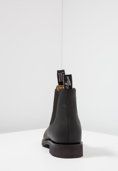 Black leather Chelsea boot with elastic side panels, flat rubber sole, and pull tabs on the heel. Smooth texture and minimalist design.