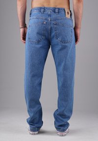 Blaue Jeans aus Denim mit lockerem Schnitt, sichtbaren Nähten, zwei Gesäßtaschen und einem Leder-Logo-Patch, kombiniert mit Low-Top Leinen-Sneakern.