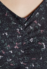 Tecido preto com um padrão abstrato subtil em verde, rosa e branco. Apresenta um decote em V e detalhe de franzido na costura central.